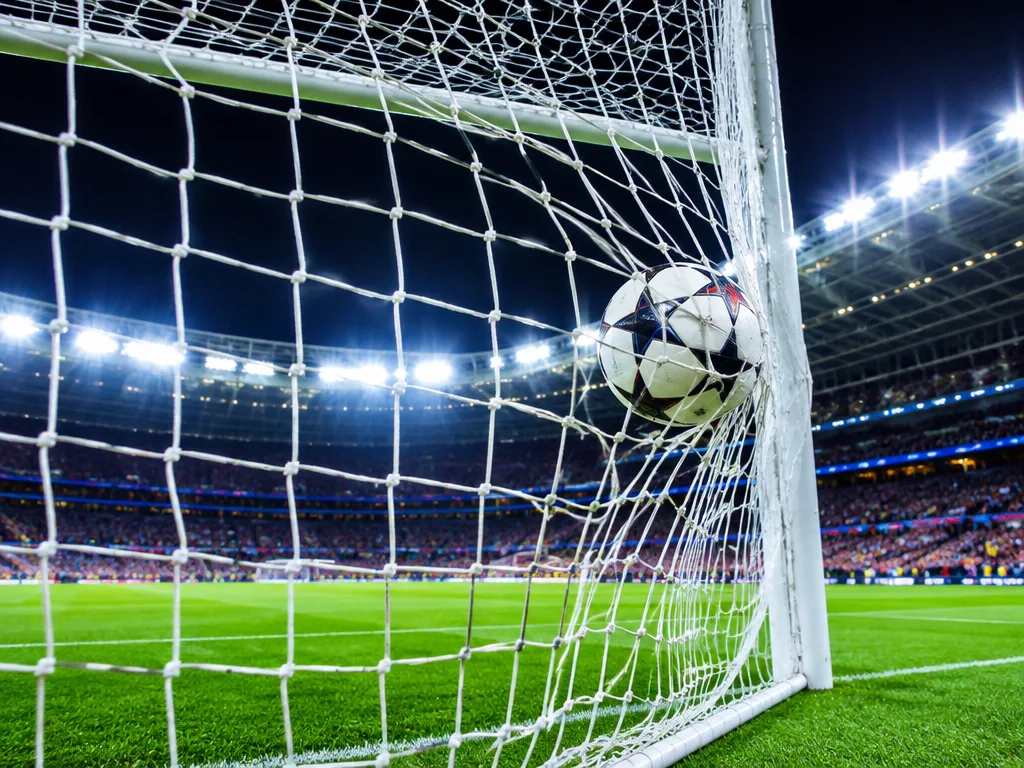 Fotboll som slår i nätet under starkt strålkastarljus på en stor fotbollsarena under en kvällsmatch